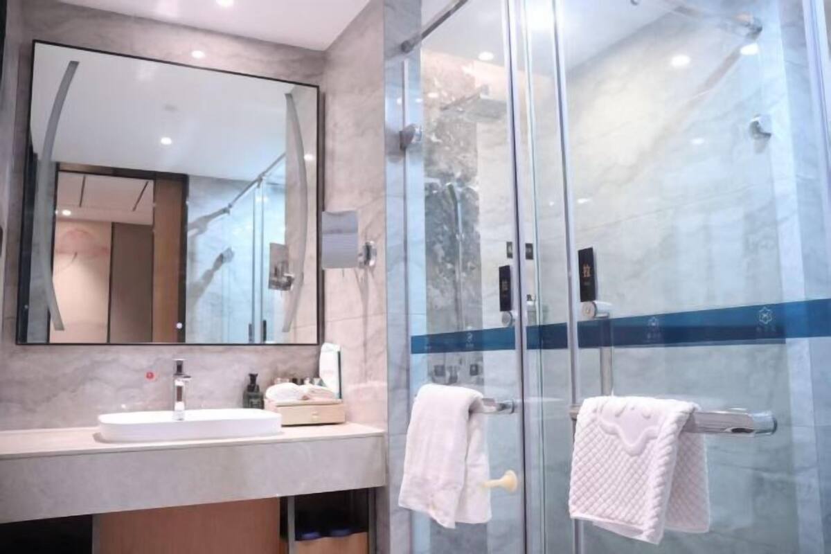 A modern bathroom with a glass shower enclosure, a large mirror, and a marble countertop.
