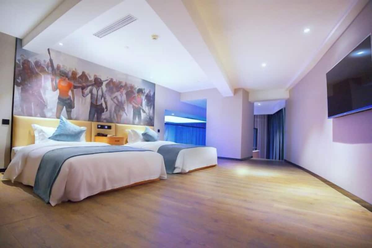 A hotel room with two beds, a large painting on the wall, a TV mounted on the wall, and a wooden floor.