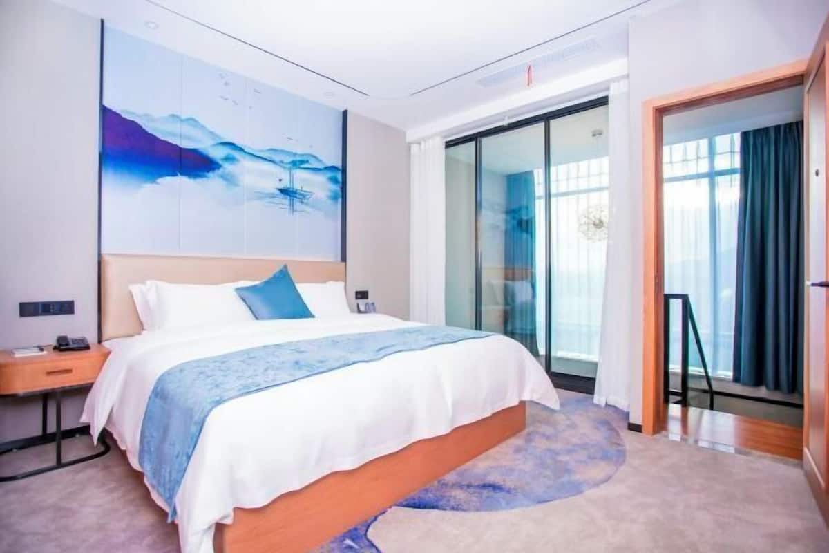 A modern hotel room with a large bed, a painting on the wall, a sliding door, and a view of the outdoors.
