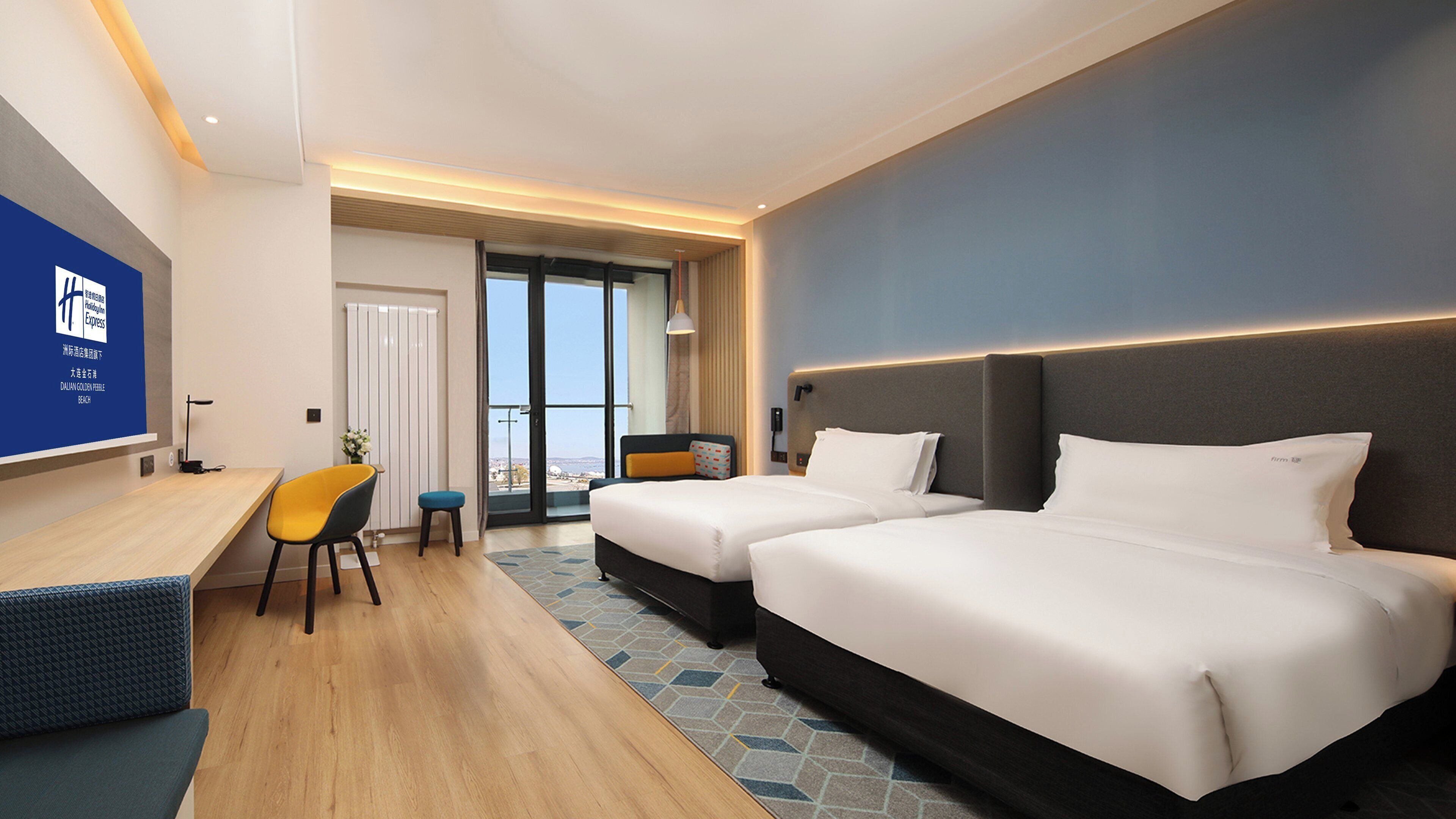 Ein Hotelzimmer mit zwei Betten, einem Schreibtisch, einem Stuhl und Blick auf die Stadt.