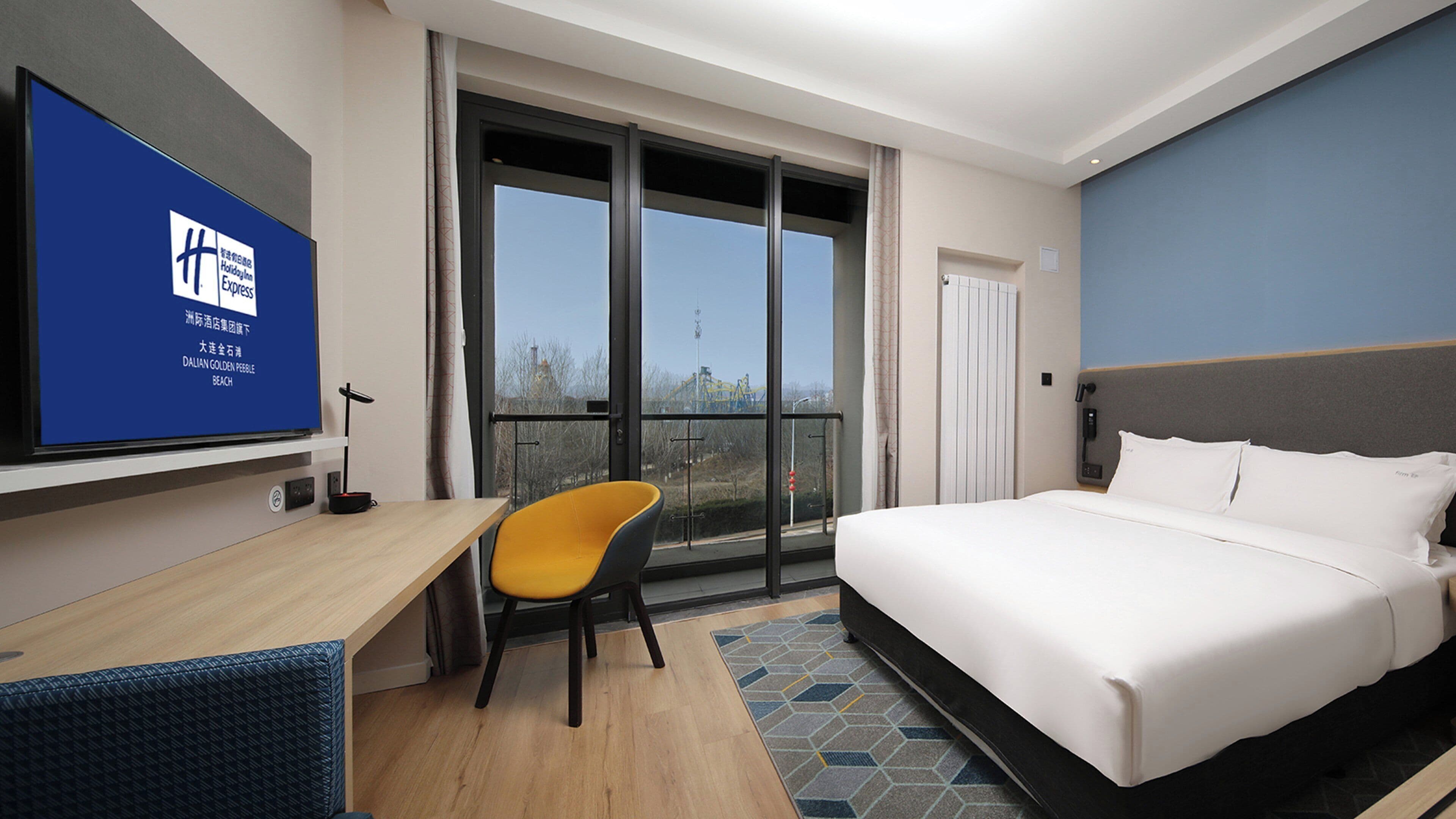 Een hotelkamer met een bed, een bureau, een stoel, een televisie en een balkon met uitzicht.