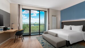 Une chambre d’hôtel moderne dotée d’un grand lit, d’un bureau avec une chaise, d’une télévision et d’un balcon offrant une vue sur la ville.