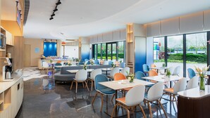 Un restaurant moderne doté d’un bar, de tables et de chaises, et de grandes fenêtres offrant une vue sur l’extérieur.