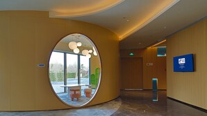 Un hall d’hôtel moderne avec un mur incurvé, un grand miroir rond et un comptoir d’accueil.