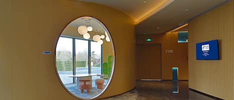 Un moderno vestíbulo de hotel con una pared curva, un espejo redondo y un mostrador de recepción.