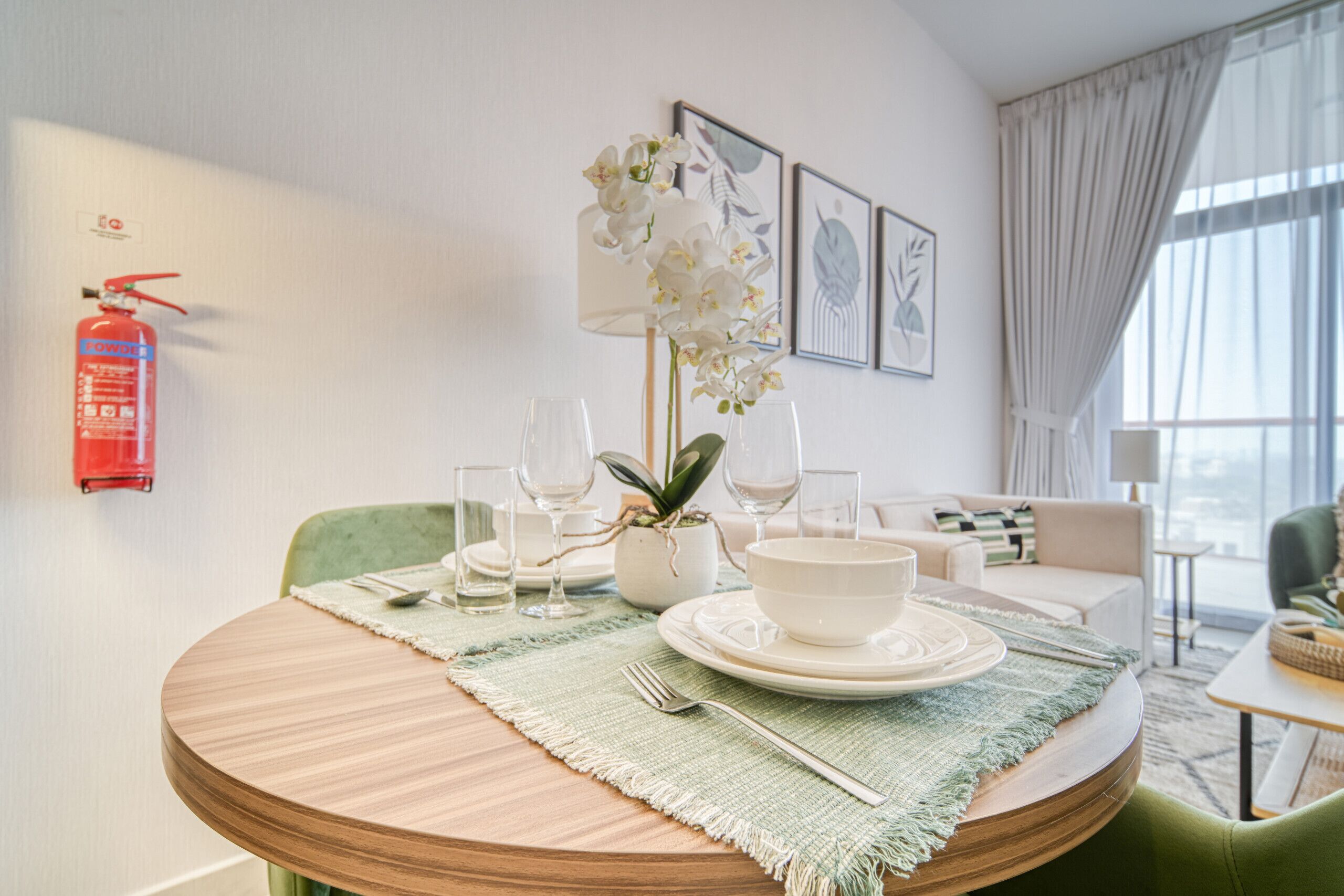 Un coin repas avec une table ronde dressée pour quatre personnes, une orchidée en pot et un extincteur fixé au mur.