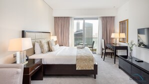 A modern hotel room with a large bed, a desk, a chair, a TV, and a balcony with curtains.