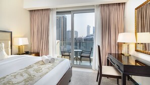 A hotel room with a large bed, a desk, and a chair. There is a balcony with a view of the city.
