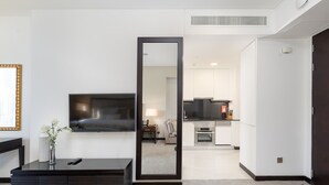 A modern hotel room with a large mirror, a flat-screen TV, a small dining table, and a kitchenette.