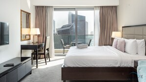 Une chambre d’hôtel avec un grand lit, un bureau avec une chaise, une télévision et un balcon offrant une vue sur la ville.