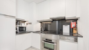 Une cuisine moderne avec des meubles blancs, des appareils en acier inoxydable, un plan de travail noir et une couverture anti-feu accrochée au mur.