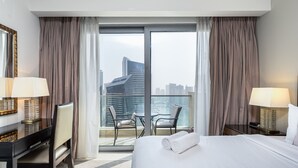 Une chambre d’hôtel avec un lit, deux chaises, un bureau et une grande fenêtre avec des rideaux.