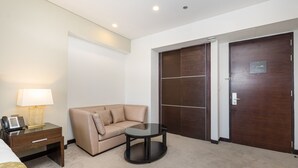 Habitación de hotel con sofá color beige, una mesita redonda pequeña, una lámpara de noche, un teléfono y un armario con espejo.