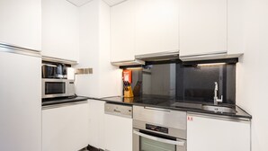 Una cocina moderna con armarios blancos, un microondas de acero inoxidable, un horno empotrado y una encimera negra.