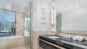 Un baño moderno con cabina de ducha de vidrio, un espejo grande y tocador con encimera negra y lavamanos blanco.