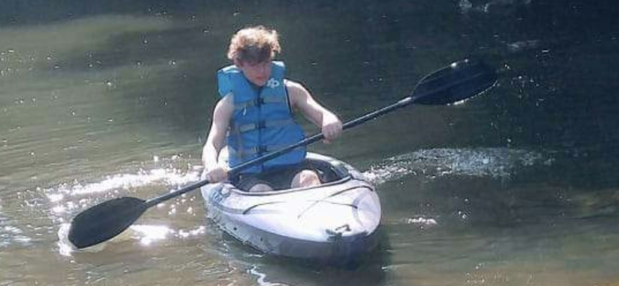 Eine Person paddelt mit einem Kajak auf einem ruhigen Fluss.