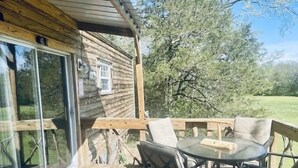 A wooden cabin with a glass door and a deck area with outdoor furniture. - Prairie Creek Cabin -Ride SxS to trails from the cabin! Kayak and Fish the Creek (Mena)