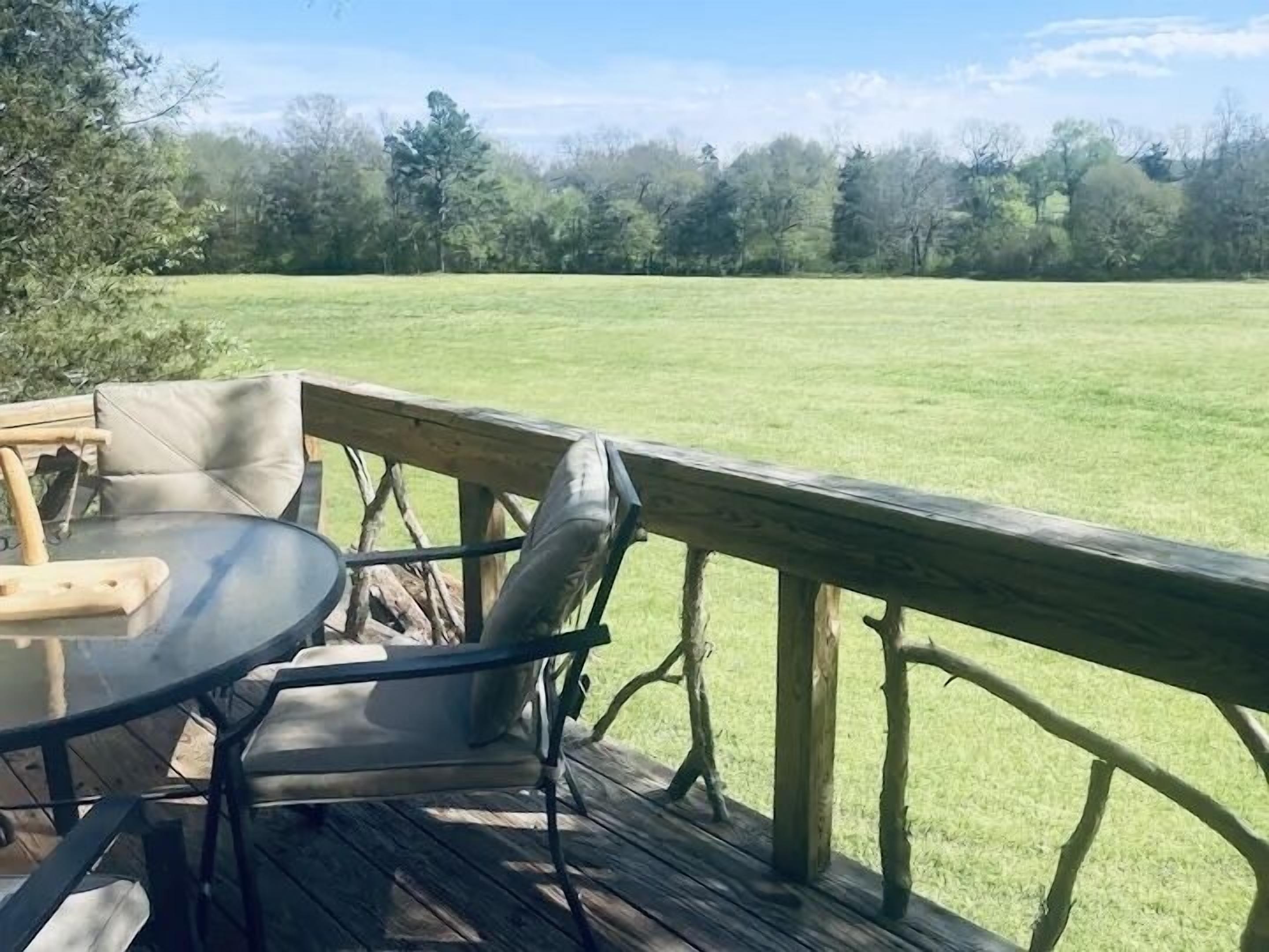 A wooden deck with a table and chairs, overlooking a grassy field.