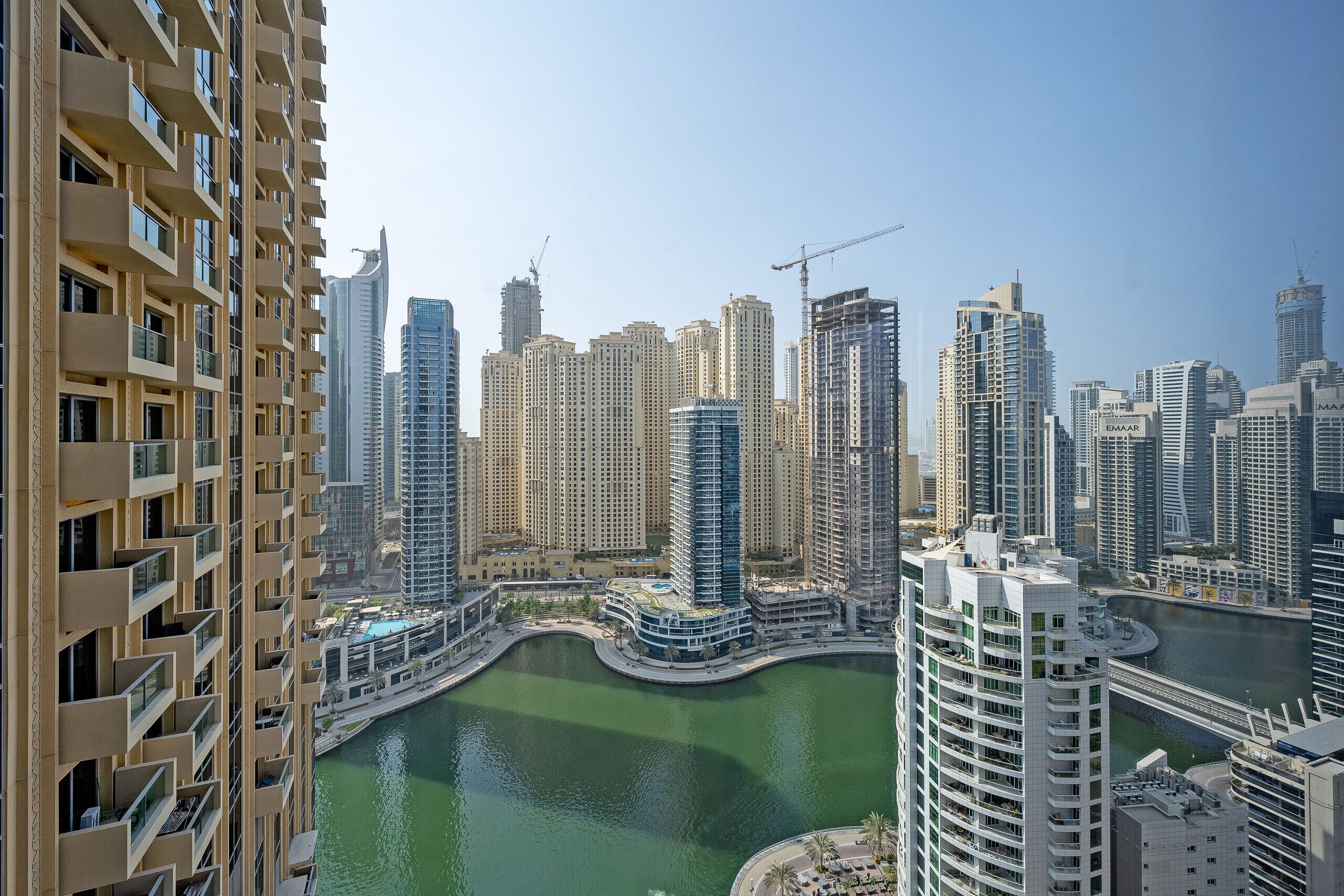 A high-rise building with multiple balconies and a view of a cityscape with other tall buildings and a body of water.