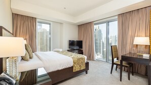 A hotel room with a bed, a desk, a chair, a TV, and large windows offering a city view. - Elegant 1BR in The Address Residences Dubai Marina by Deluxe Holiday Homes (Dubai)