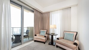 A hotel room with a balcony, two armchairs, a small round table, and a lamp.