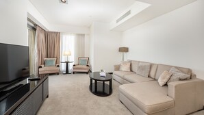 A modern hotel room with a flat-screen TV, a beige sofa, a small coffee table, and a lamp.