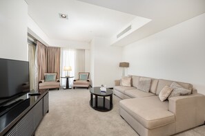 A modern hotel room with a flat-screen TV, a beige sofa, a small coffee table, and a lamp.