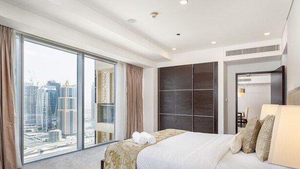 A modern hotel room with a large bed, a city view, and a sliding glass door.