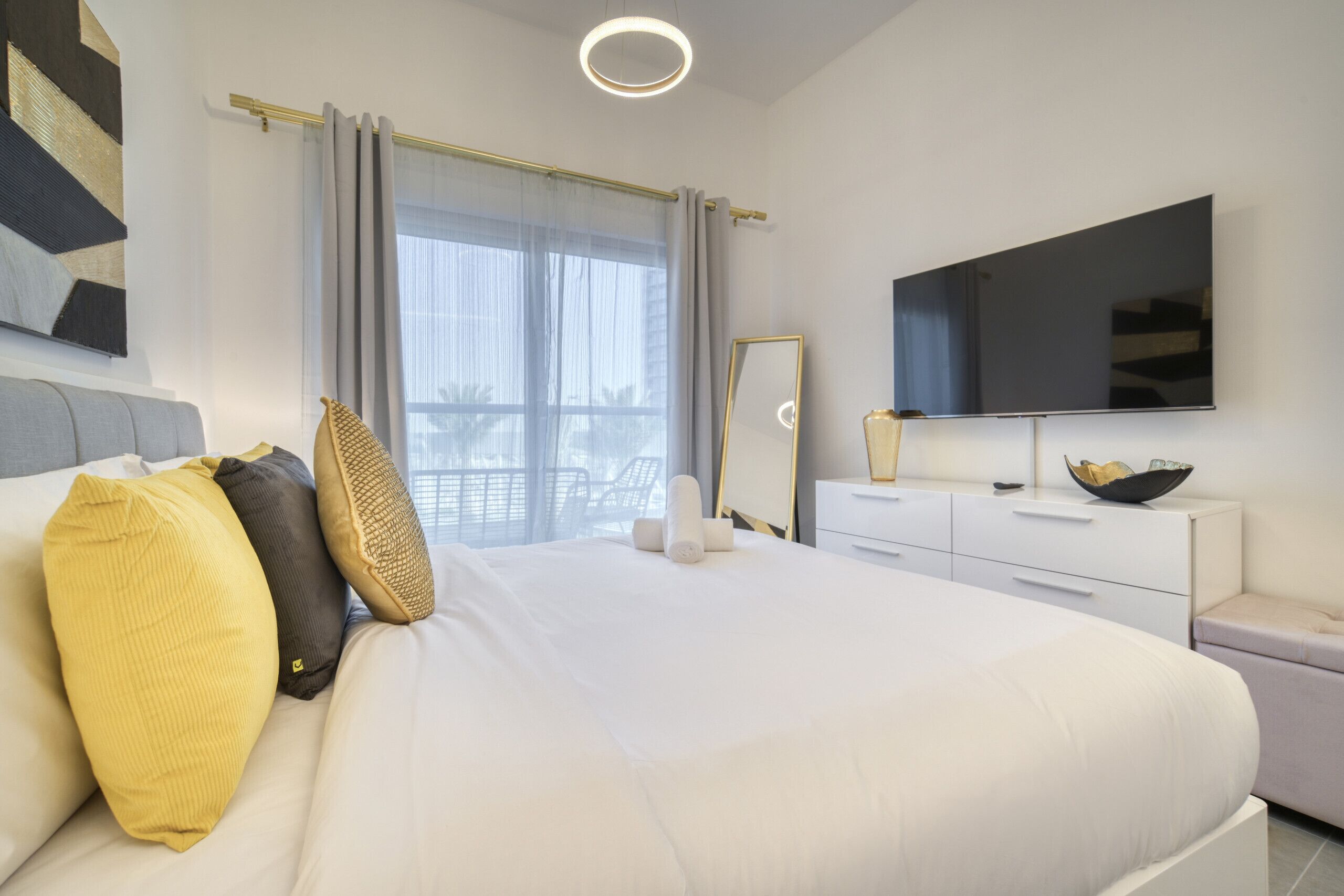 Une chambre moderne avec un grand lit, un téléviseur à écran plat, une commode et une fenêtre avec des rideaux.