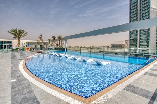 A rooftop swimming pool with clear blue water, surrounded by palm trees and modern buildings.