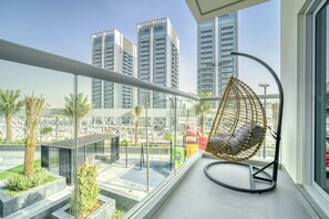 A balcony with a hanging chair, a view of tall buildings, and a landscaped area with plants.