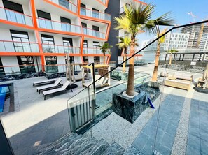 Um hotel moderno com área de piscina no terraço, espaço para sentar ao ar livre e vista para o horizonte da cidade.