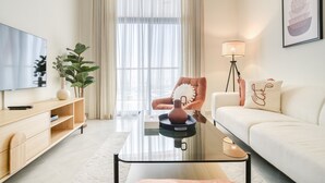 A modern living room with a sofa, a coffee table, a TV, and a large window with sheer curtains. - Homely 1BR at Binghatti Avenue Al Jaddaf by Deluxe Holiday Homes (Dubai)