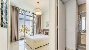 A modern bedroom with a large bed, a ceiling light, and a view of the outdoors. - Flawless 3BR Townhouse with Asst's Rm at DAMAC Hills 2 Amazonia by Deluxe Holiday Homes (Dubai)