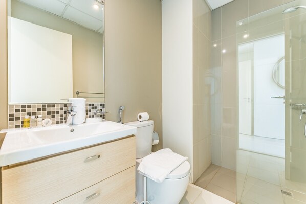 A modern bathroom with a large mirror, a sink with toiletries, a toilet, and a glass-enclosed shower area.