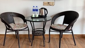 A room with a TV mounted on the wall, a round glass table with two wicker chairs, a kettle, and bottled water. - A Rest in Xinchang (Xinchang)