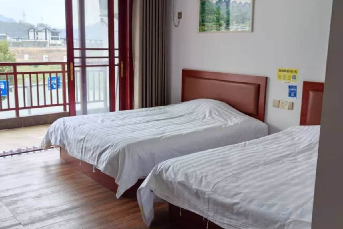 A hotel room with two beds, a wooden floor, a balcony with a view, and a painting on the wall.