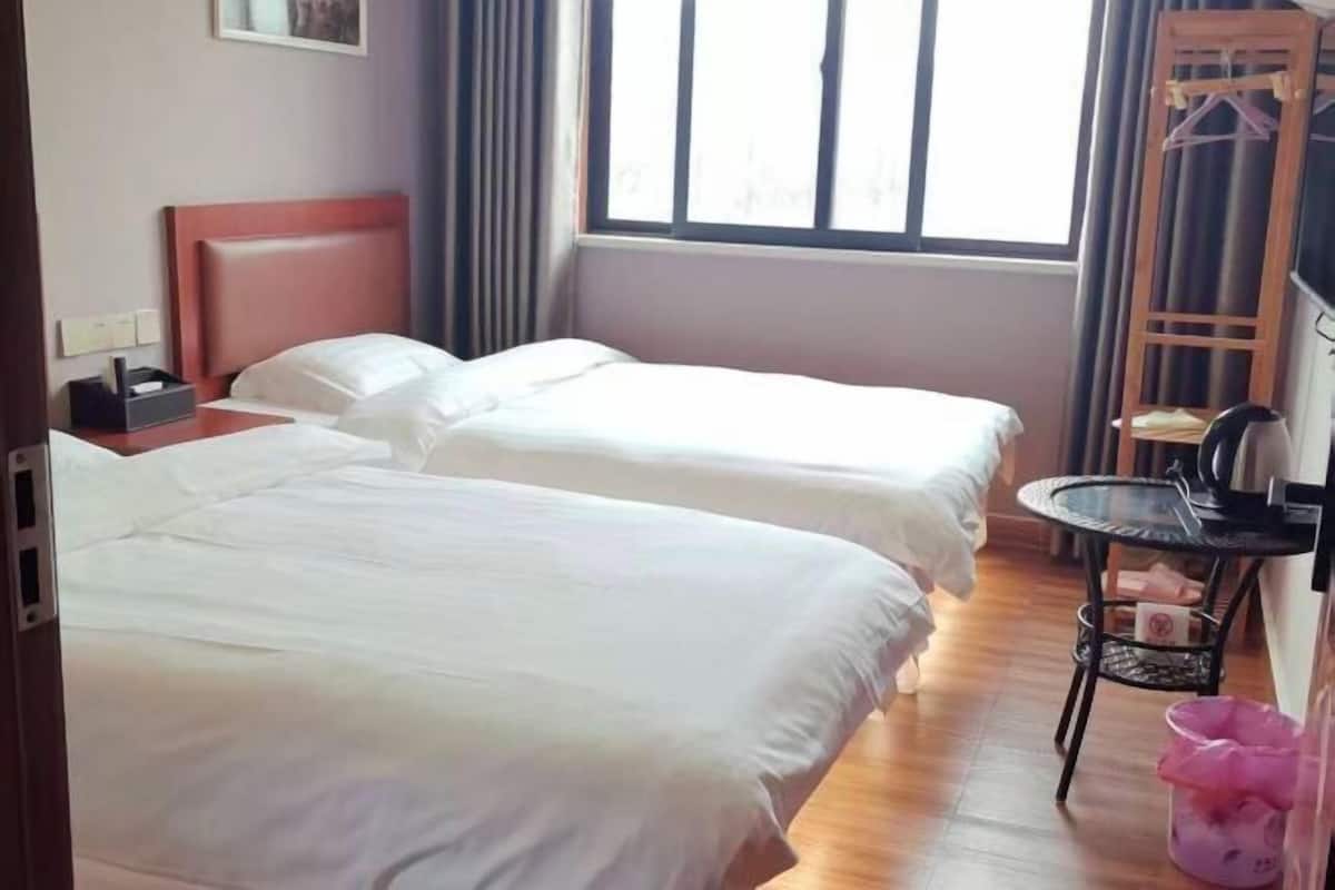 Habitación de hotel con dos camas, una mesita, una silla, una ventana y un perchero.