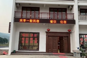 Un edificio de dos pisos con un balcón, un amplio puerta de entrada y un letrero con caracteres chinos.