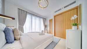 Ein modernes Schlafzimmer mit einem großen Bett, einem Nachttisch, einer Kommode, einem Spiegel, einem Fenster mit Vorhängen und einer Deckenleuchte.