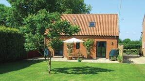 Une maison en briques avec un toit en tuiles, une terrasse avec une table et des chaises, et un petit jardin.