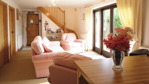 Un salon chaleureux avec un escalier en bois, un canapé rose, une table basse en bois et un vase rempli de fleurs.