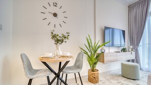 Uma sala moderna com área de jantar, um relógio de parede grande, televisão de tela plana e uma janela ampla com cortinas.