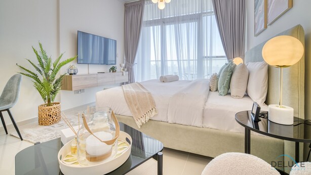 Quarto moderno com uma cama grande, televisão de tela plana, mesa de cabeceira, planta em vaso e janela com cortinas.