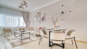 A modern living room with a sofa, coffee table, dining table, and chairs. There are wall art pieces and a unique wall clock.