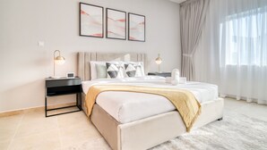 A modern bedroom with a large bed, a nightstand, a lamp, and a window with curtains.