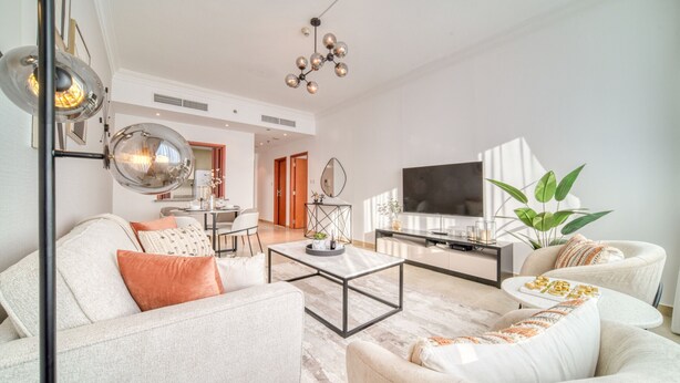 A modern living room with a sofa, armchairs, a coffee table, and a TV. There is a dining area in the background with a table and chairs.