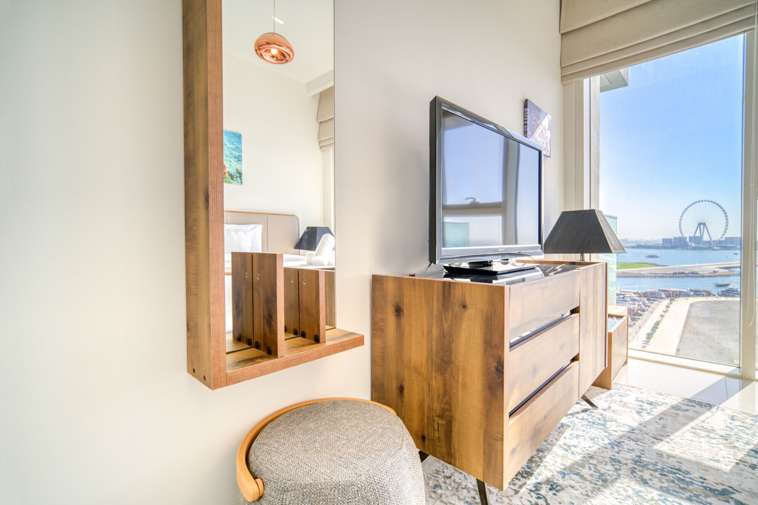 A modern hotel room with a large window offering a view of a Ferris wheel and water body.