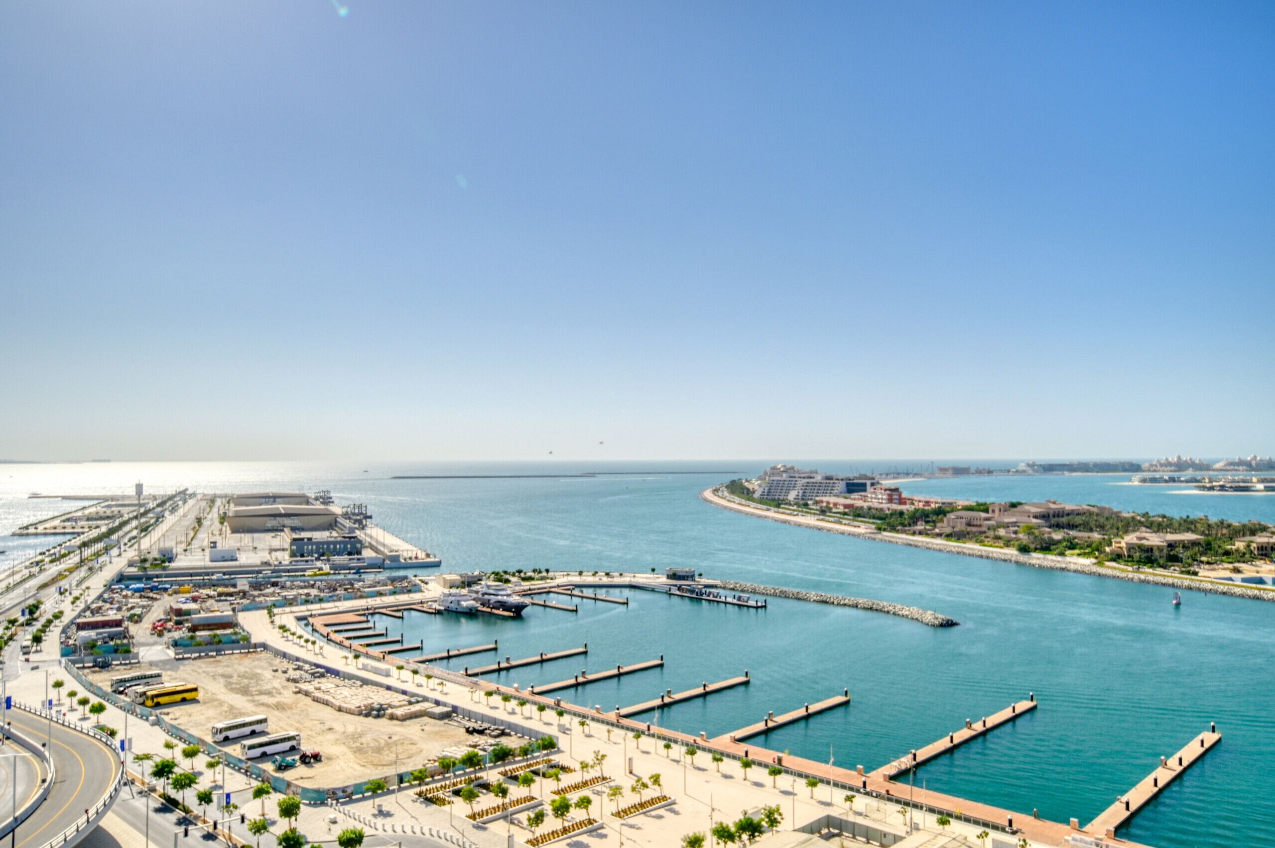 Rannikolla sijaitseva venesatama, jossa on laiturit, hiekkaranta ja kirkas, sininen taivas.