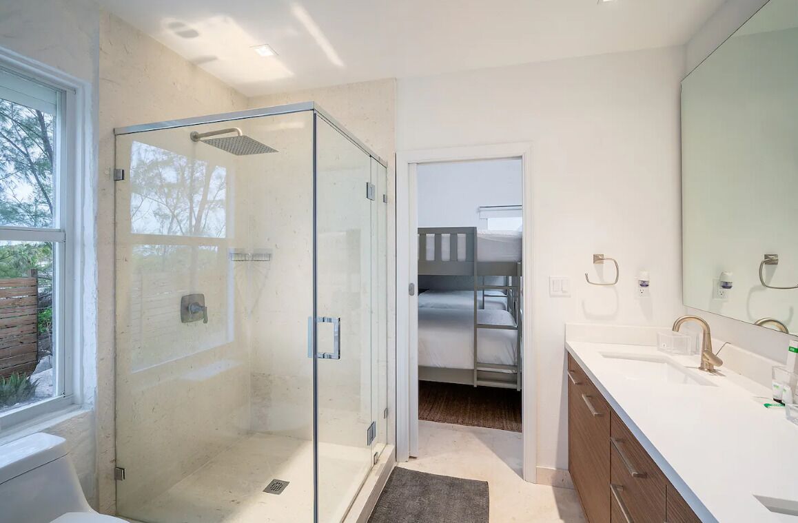 Een moderne badkamer met een douchecabine van glas, een grote spiegel en een wit wastafelmeubel.